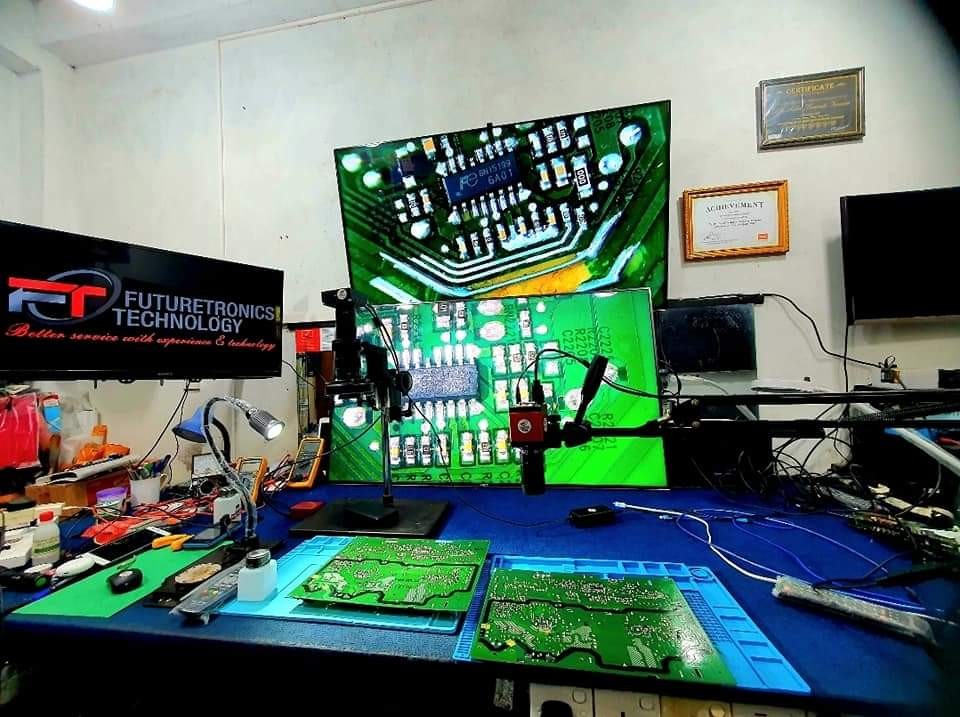 Precision soldering station with microscope focused on a green TV logic board.